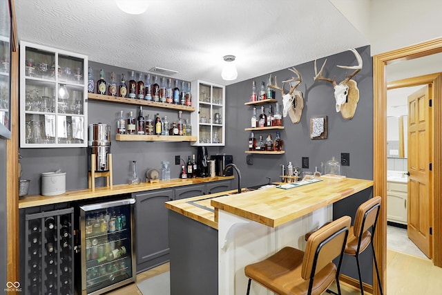 bar with a sink, indoor wet bar, a textured ceiling, and beverage cooler