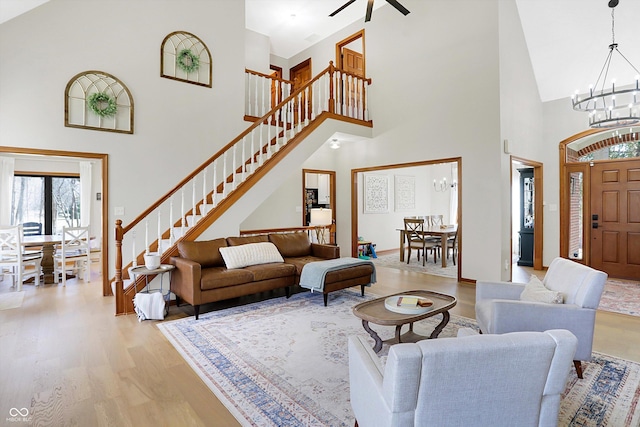 living area featuring stairway, an inviting chandelier, light wood-style flooring, and a towering ceiling