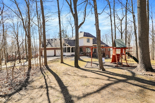 rear view of house featuring a playground, an attached garage, brick siding, and dirt driveway