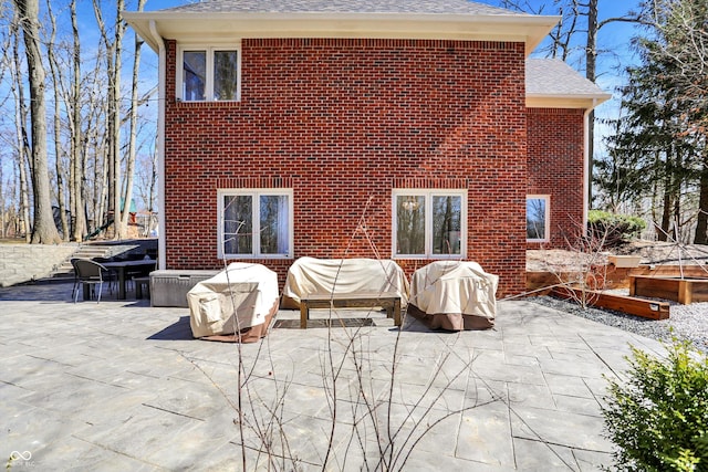 back of property featuring brick siding, a patio area, an outdoor hangout area, and roof with shingles