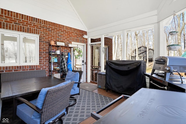 home office with wood finished floors, plenty of natural light, brick wall, and vaulted ceiling