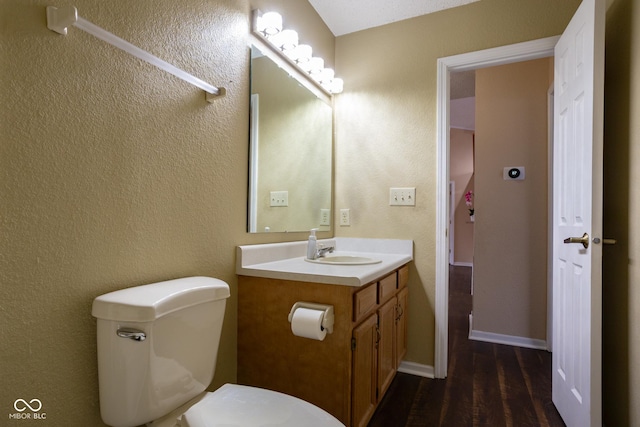 half bathroom with a textured wall, toilet, vanity, wood finished floors, and baseboards