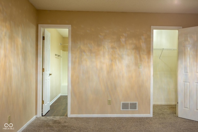 unfurnished bedroom with visible vents, a walk in closet, a closet, and carpet flooring