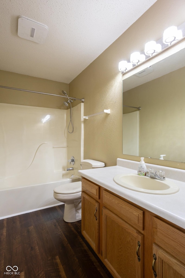 full bath featuring a textured ceiling, toilet, wood finished floors, vanity, and shower / bathing tub combination