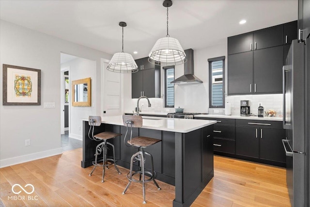 2026 Alvord St, Indianapolis, IN 46202 - kitchen with dark cabinetry, light wood-style flooring, freestanding refrigerator, light countertops, and wall chimney range hood