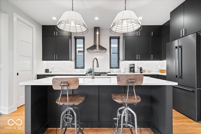 2026 Alvord St, Indianapolis, IN 46202 - kitchen with light wood finished floors, wall chimney range hood, light countertops, high end refrigerator, and dark cabinetry