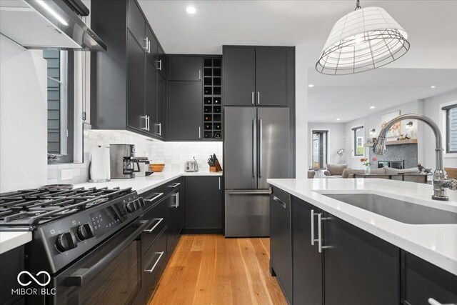 2026 Alvord St, Indianapolis, IN 46202 - kitchen with wall chimney range hood, dark cabinets, black range with gas cooktop, high end fridge, and a sink