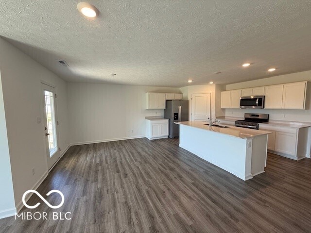 kitchen with white cabinets, stainless steel appliances, dark wood-type flooring, a center island with sink, and a textured ceiling