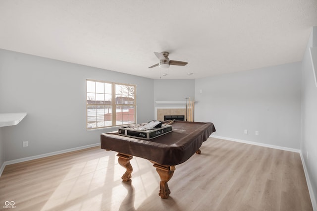 recreation room with a tile fireplace, baseboards, ceiling fan, and light wood finished floors