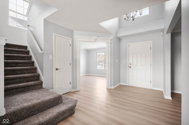 entryway with a textured ceiling, light wood-style flooring, baseboards, and stairs