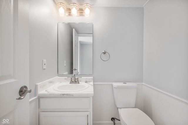 half bath with a wainscoted wall, vanity, and toilet