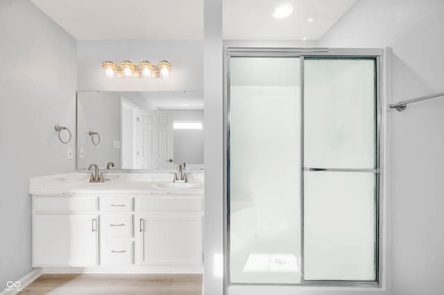 full bathroom featuring double vanity, a shower with door, a sink, and wood finished floors