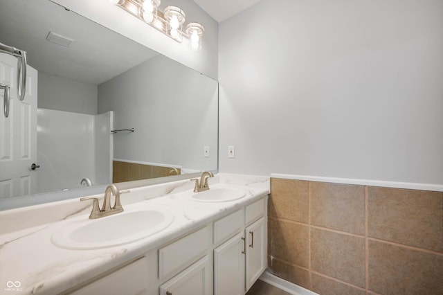 bathroom with double vanity, wainscoting, a sink, and tile walls