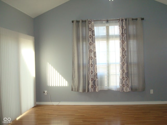 unfurnished room featuring a healthy amount of sunlight, baseboards, wood finished floors, and lofted ceiling