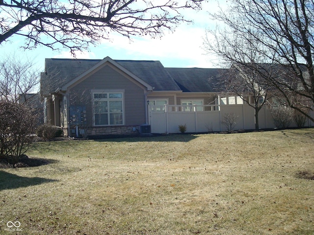 view of front of home featuring a front yard, stone siding, fence, and central AC unit