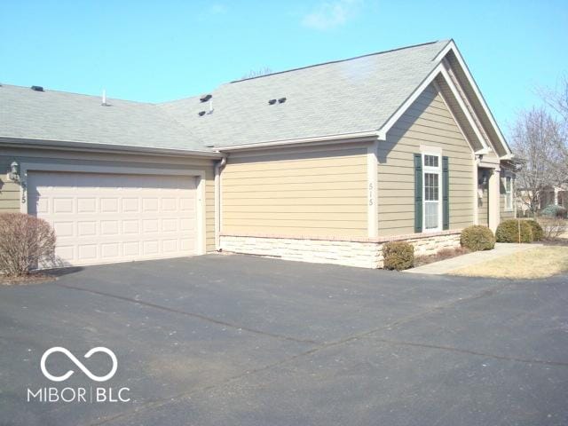 view of side of home with aphalt driveway, roof with shingles, and an attached garage