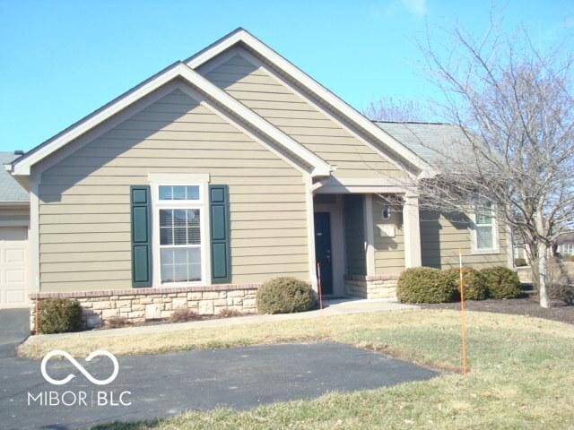 view of front facade featuring a garage, a front yard, stone siding, and driveway