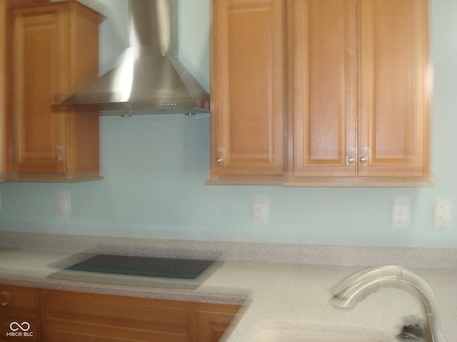 kitchen with light countertops, a sink, wall chimney range hood, and black electric stovetop