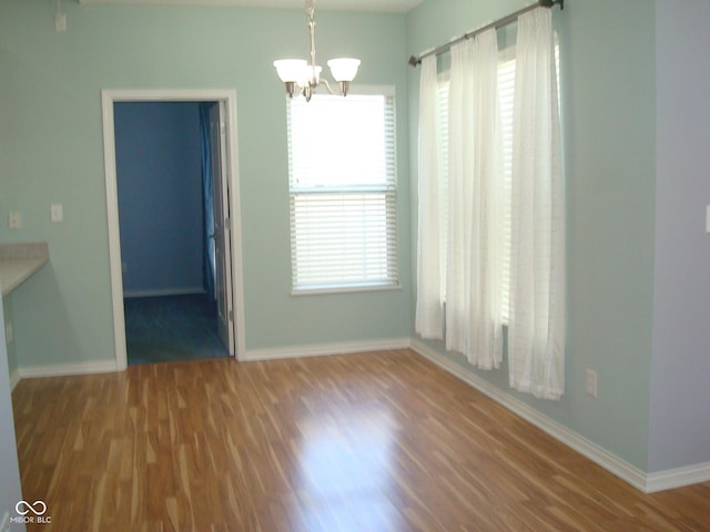 unfurnished dining area with a chandelier, wood finished floors, and baseboards