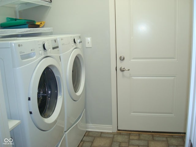 laundry area featuring stone finish floor, laundry area, washing machine and dryer, and baseboards