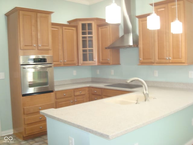 kitchen featuring a peninsula, wall chimney range hood, light countertops, and oven