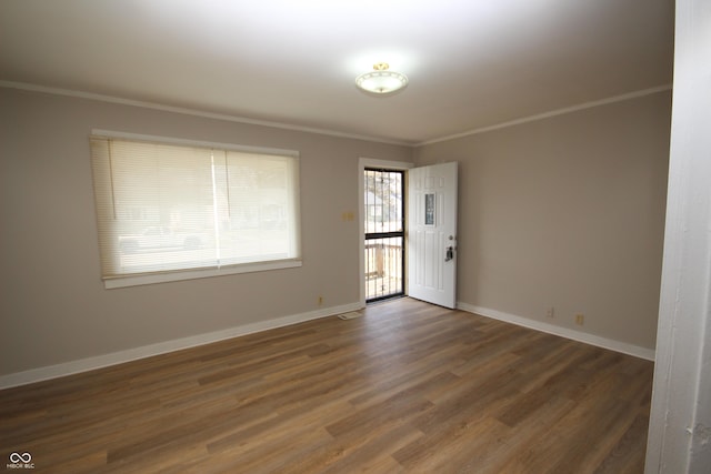 empty room featuring crown molding, baseboards, and wood finished floors