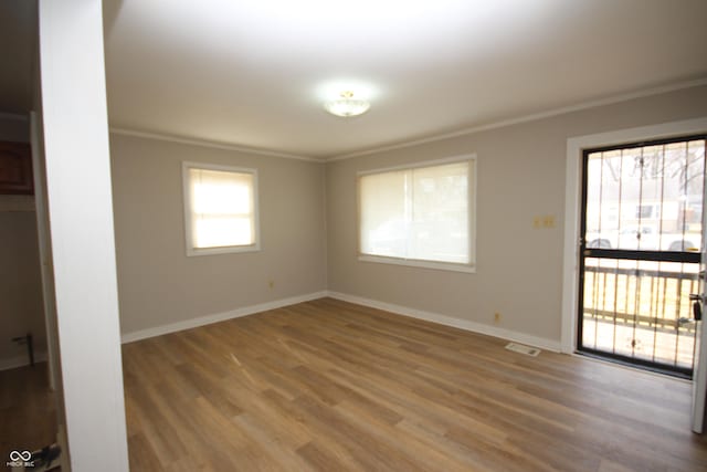 empty room featuring baseboards, crown molding, and wood finished floors