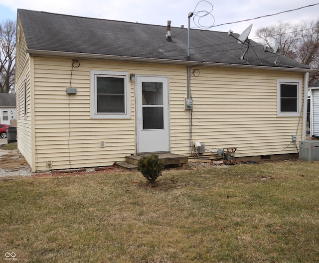 rear view of house with central AC, a shingled roof, and a lawn