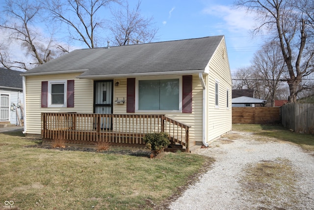 bungalow featuring a shingled roof, covered porch, fence, driveway, and a front lawn