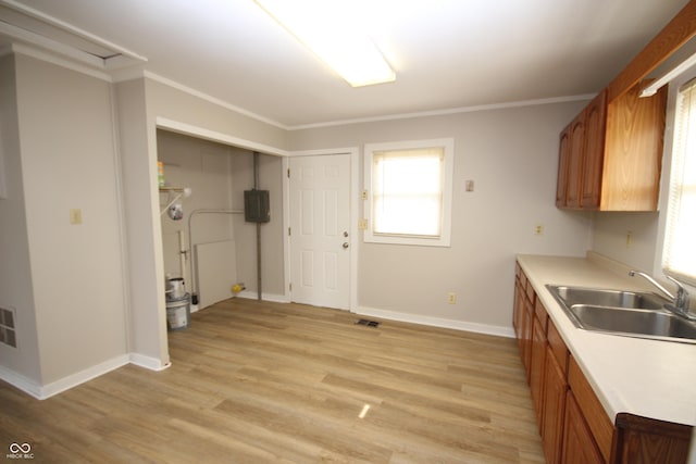 kitchen featuring light wood-style flooring, crown molding, brown cabinetry, and a sink