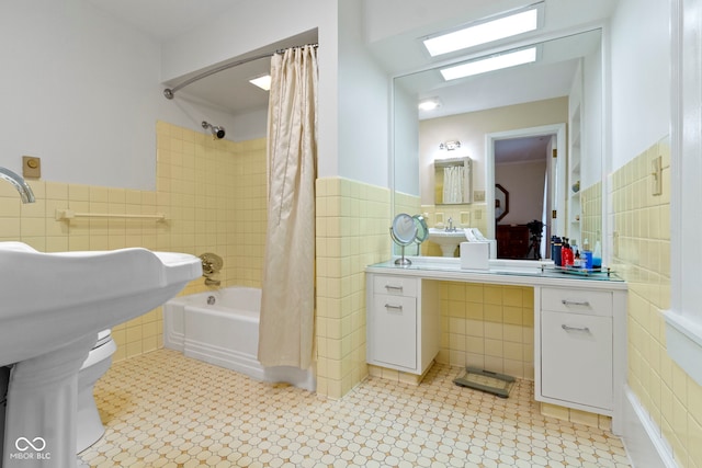 full bath featuring a sink, shower / bathtub combination with curtain, tile walls, and a wainscoted wall