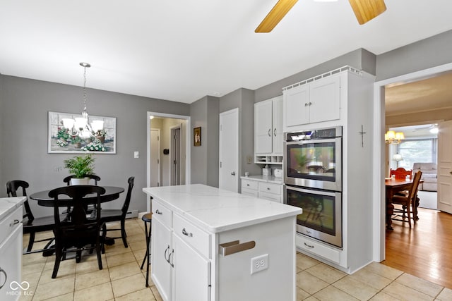 kitchen with a center island, light tile patterned floors, ceiling fan with notable chandelier, stainless steel double oven, and white cabinets