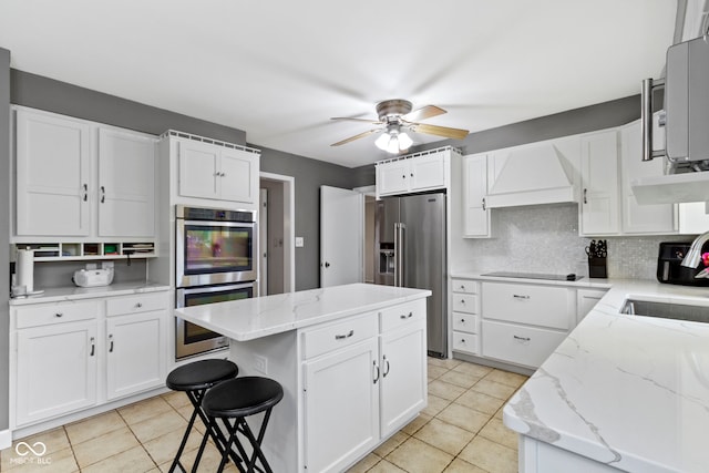 kitchen featuring light tile patterned floors, custom exhaust hood, stainless steel appliances, white cabinets, and tasteful backsplash