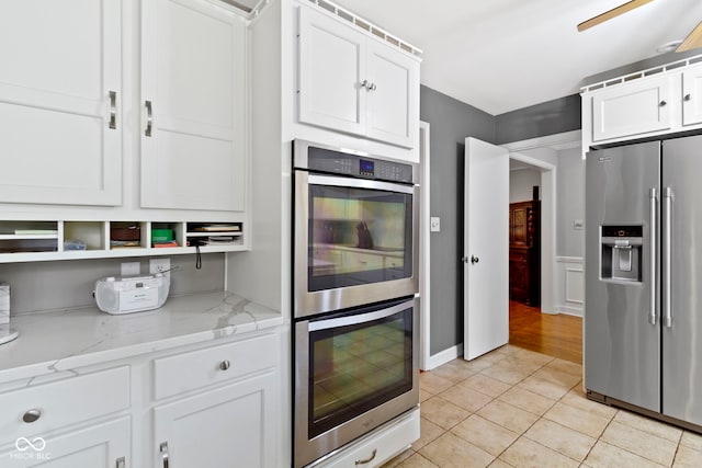 kitchen with light tile patterned flooring, white cabinetry, stainless steel appliances, and light stone counters