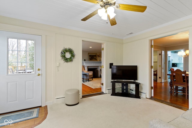 living area featuring crown molding, carpet floors, ceiling fan with notable chandelier, a fireplace, and a baseboard radiator