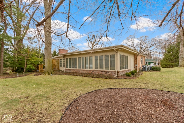 rear view of property featuring a sunroom, brick siding, a chimney, and a lawn