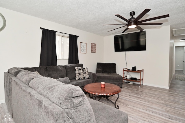 living area featuring a textured ceiling, light wood-style flooring, a ceiling fan, baseboards, and attic access