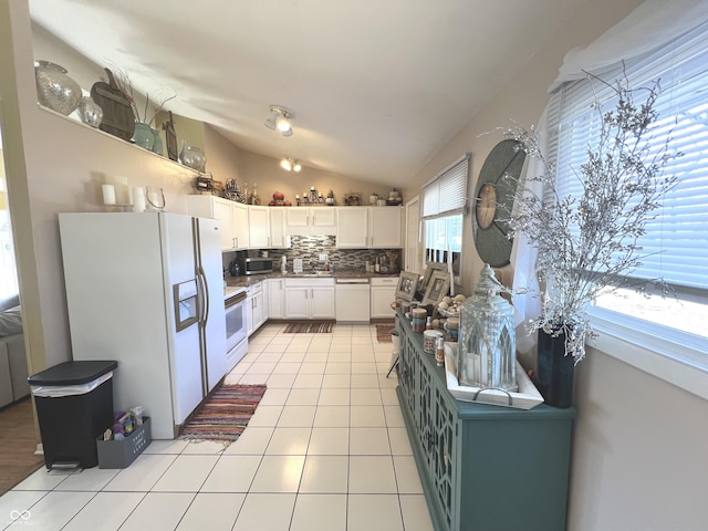 kitchen with backsplash, white appliances, white cabinets, light tile patterned floors, and lofted ceiling