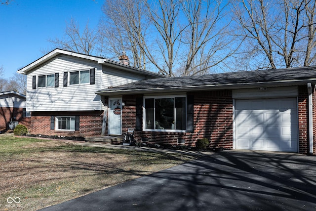 split level home with aphalt driveway, an attached garage, brick siding, and a chimney