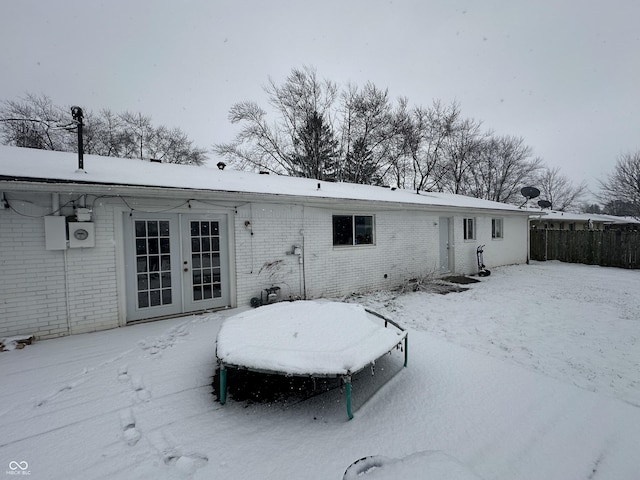 snow covered house featuring french doors and brick siding