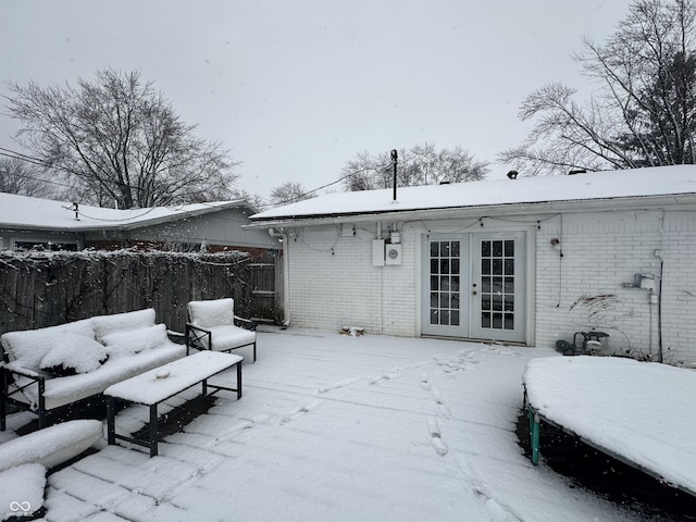 snow covered patio with a garage, french doors, and fence