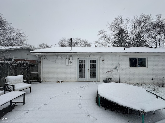 snow covered back of property with french doors and brick siding