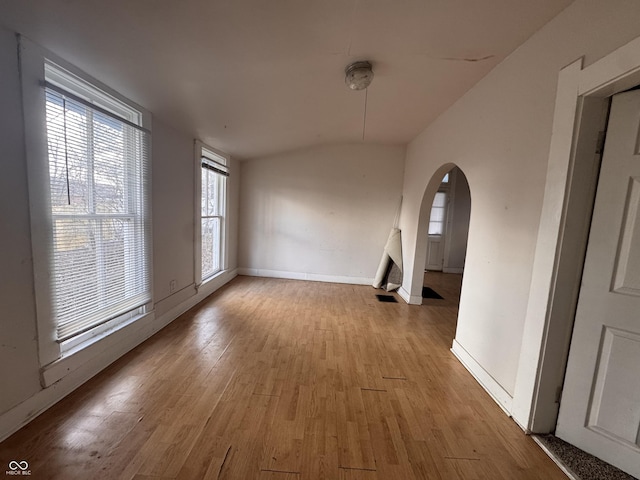 interior space featuring vaulted ceiling, wood finished floors, arched walkways, and baseboards