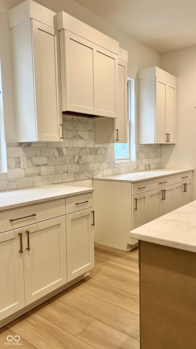 kitchen featuring light countertops, tasteful backsplash, light wood-style flooring, and white cabinets