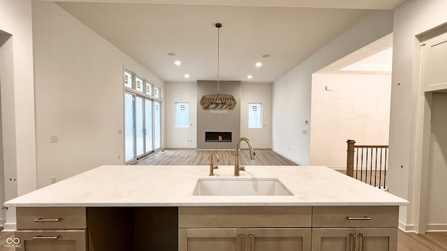 kitchen with light stone counters, light wood-style flooring, a fireplace, a sink, and open floor plan