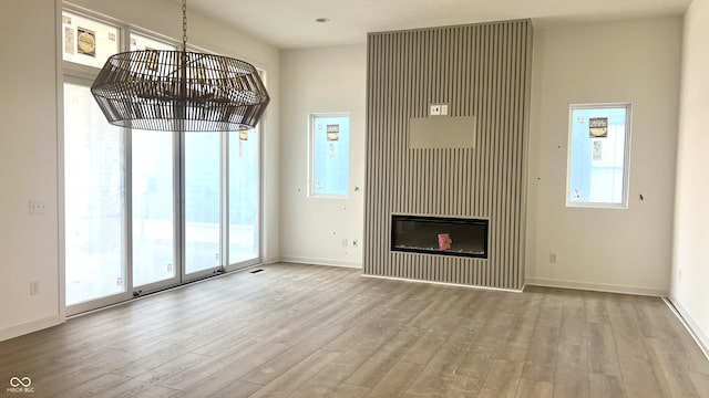 unfurnished living room with a wealth of natural light, baseboards, wood finished floors, and a glass covered fireplace