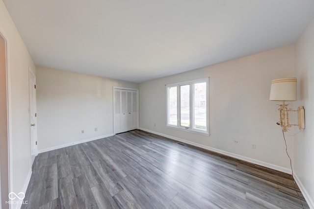 unfurnished room featuring dark wood-style flooring, visible vents, and baseboards