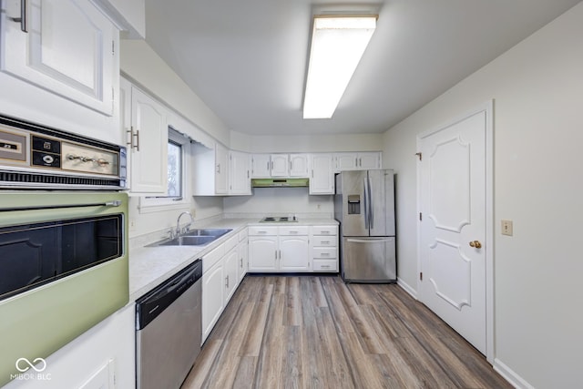 kitchen with under cabinet range hood, appliances with stainless steel finishes, white cabinets, and a sink