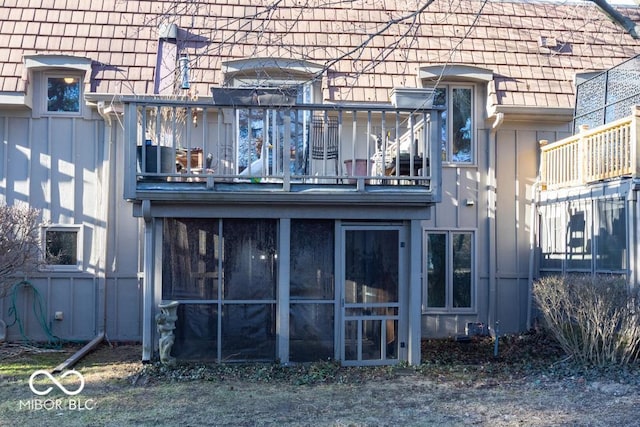 rear view of house with a balcony, a sunroom, and board and batten siding