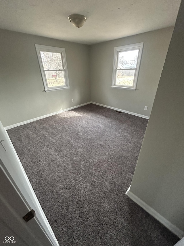 unfurnished room featuring plenty of natural light, dark carpet, and baseboards